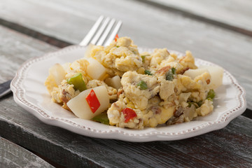 Scrambled eggs with Anaheim chilies, boiled potatoes, green peppers, and onions side view on a weathered barn wood table