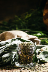 Dried sage in a glass jar, fresh sage on the vintage wooden tabl