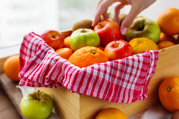 Box full of fresh fruits. Woman chooses fruits. Fruit harvest - apples, oranges, lemon, kiwi, banana. Rustic background.