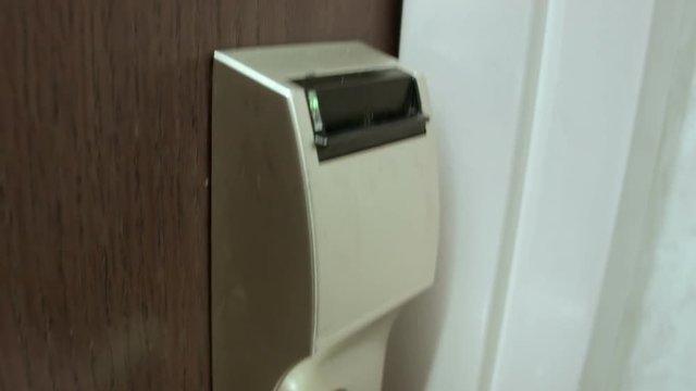 A male hand using a typical hotel keycard to unlock his hotel room door.