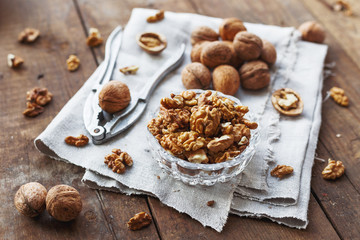 Fototapeta na wymiar Glass bowl with walnuts on rustic homespun napkin. Healthy snack on old wooden background.