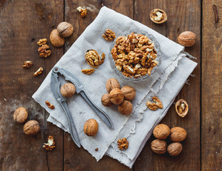 Glass bowl with walnuts on rustic homespun napkin. Healthy snack on old wooden background.