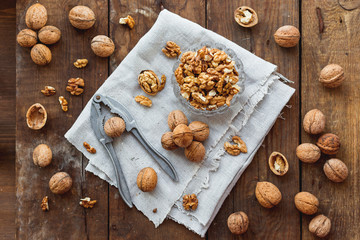 Glass bowl with walnuts on rustic homespun napkin. Healthy snack on old wooden background.