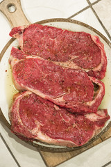 raw new york steaks on cutting board seasoned