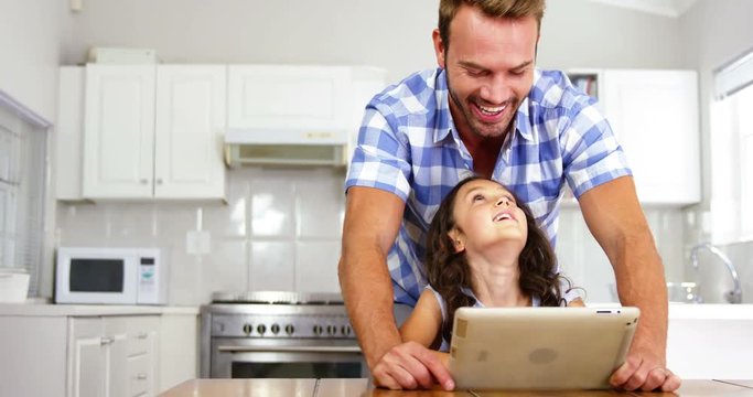 Daughter and father laughing in front of a tablet