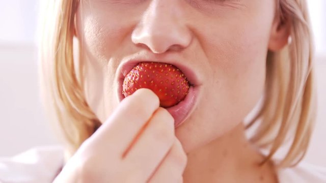 Close up on a blonde woman eating a strawberry