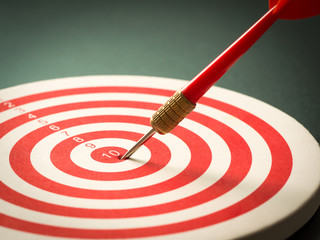 Selective focus of red dart arrow hitting target center of dartboard on black background. Bullseye...