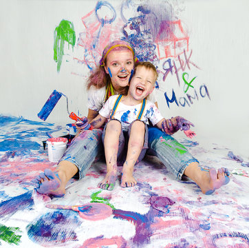 Mother and son paint the walls. Child himself dirty in the paint and looks into the camera. Child has fun and stain the wall. Children's creativity. Art for baby.