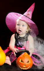 Halloween baby witch with a carved pumpkin over black background