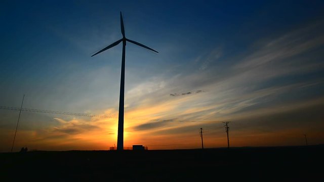 Obracająca się turbina wiatrowa produkująca prąd podczas zachodu słońca