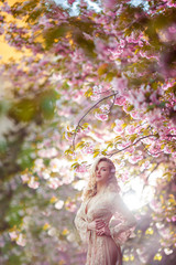 Beautiful young woman standing at blossoming tree in the garden