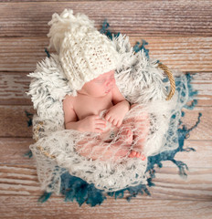 tiny newborn baby in white knitted hat on fur