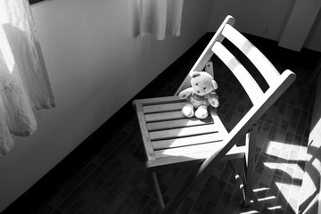 Cute teddy bear sitting alone on chair near window,black and whi