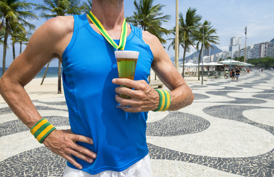 Brazilian athlete standing with first place gold medal in the shape of a glass of beer standing on Copacabana Beach in Rio de Janeiro Brazil