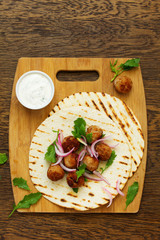 Homemade meatballs on a tortilla tacos with white sauce.