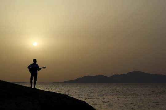 lonely figure of a man on a cliff by the sea with guitar