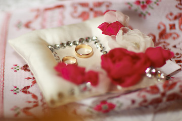 Wedding rings lie on the pillow with crystals and silk pink rose