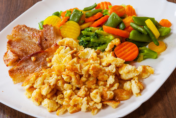 scrambled eggs with bacon and vegetables mix in a plate on wooden table