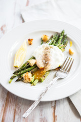 Green Griddled Asparagus with Poached Egg, Lemon and Sourdough Crumbs on a Plate, Light Background