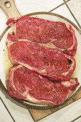 raw new york steaks on cutting board seasoned