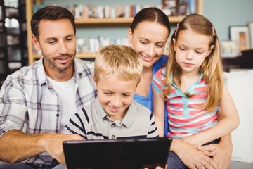 Family smiling while using technologies on sofa at home