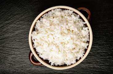 Boiled white rice in ceramic pot on black background.