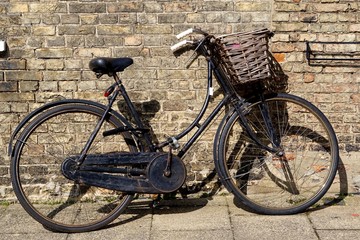 Old style black ladies' bike with wicker basket leaning against a yellow brick wall in Ely, Cambridgeshire.