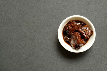 Fototapeta na wymiar Chinese red fermented tofu, a preserved condiment made from bean curd (sometimes called bean curd cheese), in a small white dipping bowl on grey background.