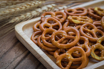 Salted pretzel on wooden plate and wheat
