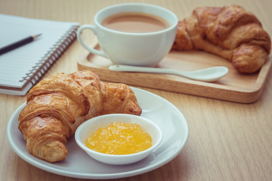 Croissant with jam on plate and coffee cup, book