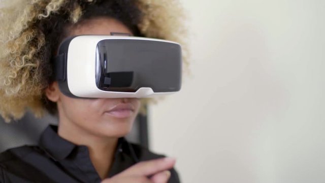 Young mixed-race businesswoman working in virtual reality by using her fingers against virtual objects while using 3d virtual reality headset.