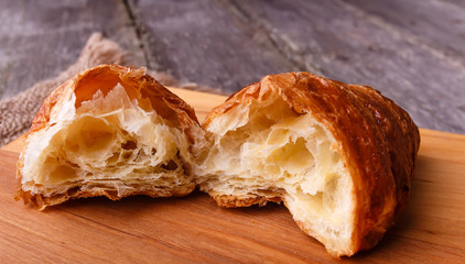 Two halfs of fresh baked different croissant on wooden table in rustic style