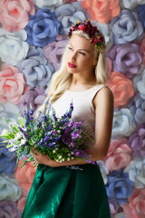 dreamy young woman in flower diadem standing with bouquet of flo