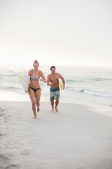 Couple with surfboard running on the beach