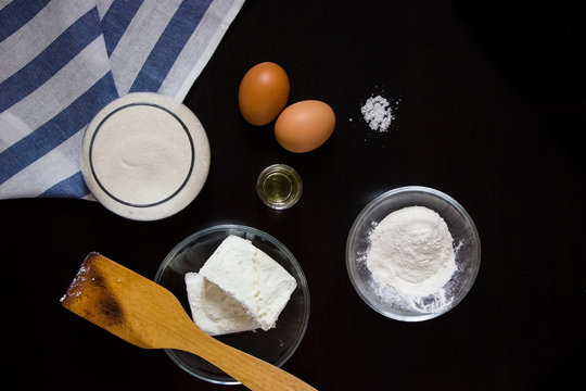 ingredients for making cottage cheese dough (cottage cheese, flour, sugar, eggs, oil, salt) on a dark background