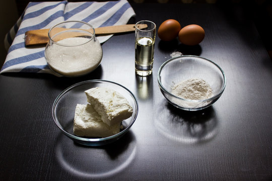 ingredients for making cottage cheese dough (cottage cheese, flour, sugar, eggs, oil, salt) on a dark background