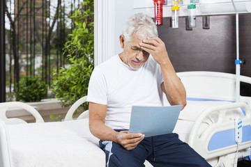 Tensed Senior Man Reading Reports In Rehab Center