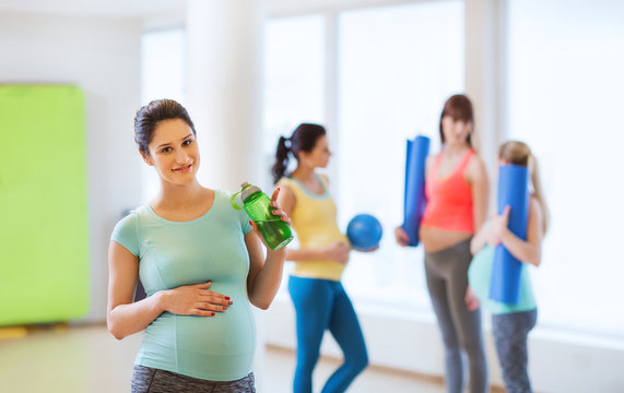 happy pregnant woman with water bottle in gym