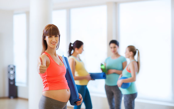 pregnant woman with mat showing thumbs up in gym