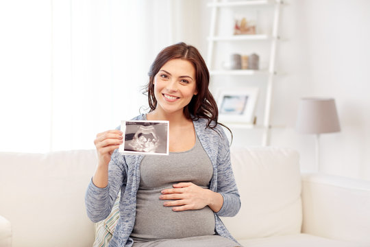 happy pregnant woman with ultrasound image at home
