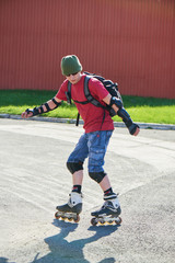 Fototapeta na wymiar The guy is going backwards on roller skates on an asphalt track against the red wall