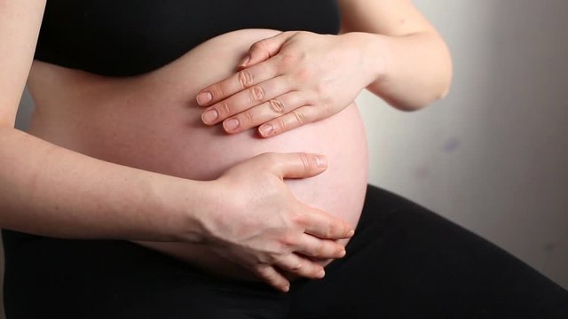 A pregnant woman stroking her belly making a heart shape with fingers
