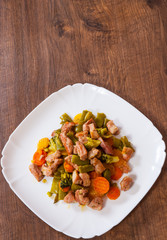 stewed meat with vegetables in a plate on wooden table
