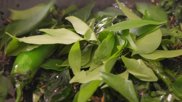 Curry leaves being thrown in a pan with spices, chillies and condiments 