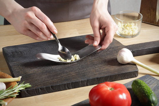 woman's hands holding a spoon and crushed garlic 