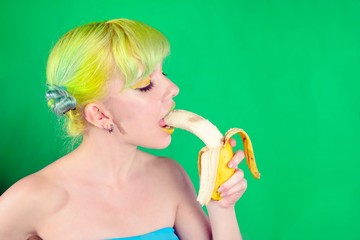 Beautiful girl with green hair eat banana on green background