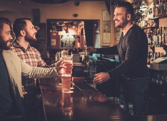 Cheerful old friends having fun and drinking draft beer at bar counter in pub.