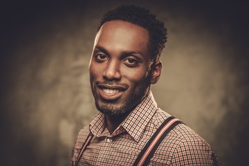 Stylish young black man with suspenders posing on dark background.