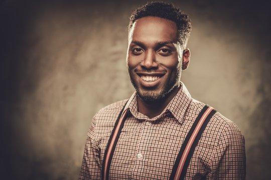 Stylish Young Black Man With Suspenders Posing On Dark Background.