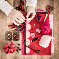 Hands of hobbyist making felt flowers - felting supplies on wooden table - high angle, square. 